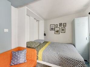 A bedroom with a bed, a wardrobe, a chair, and a wall with framed pictures. - Studio - 2P - Vieux Lyon (Lyon)