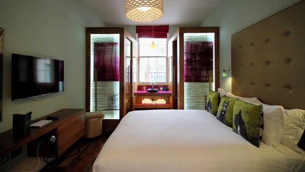 Une chambre d’hôtel avec un grand lit, un téléviseur à écran plat, une commode en bois et une fenêtre avec des rideaux.