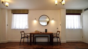 Un coin repas comprenant une table en bois, quatre chaises, un miroir rond et deux lampes fixées au mur.
