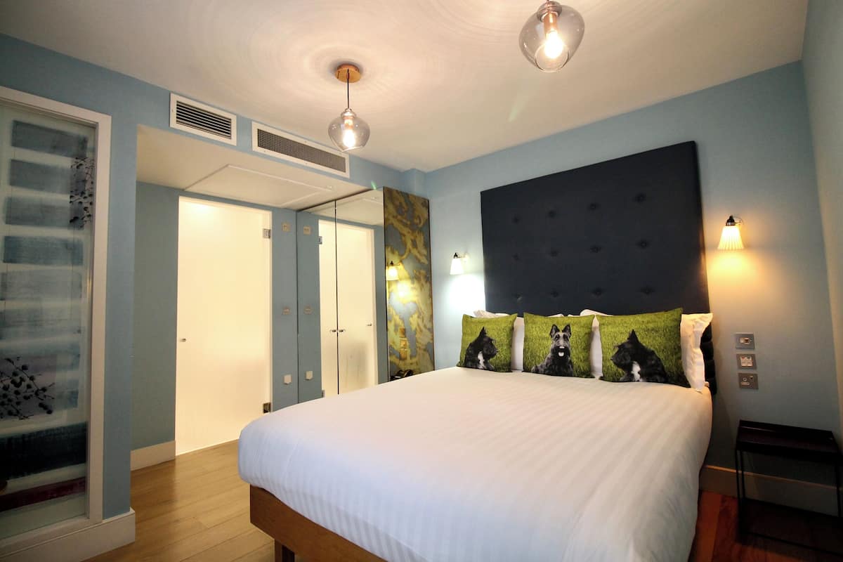 A bedroom with a large bed, a headboard with lights, a mirror, and a door leading to another room.