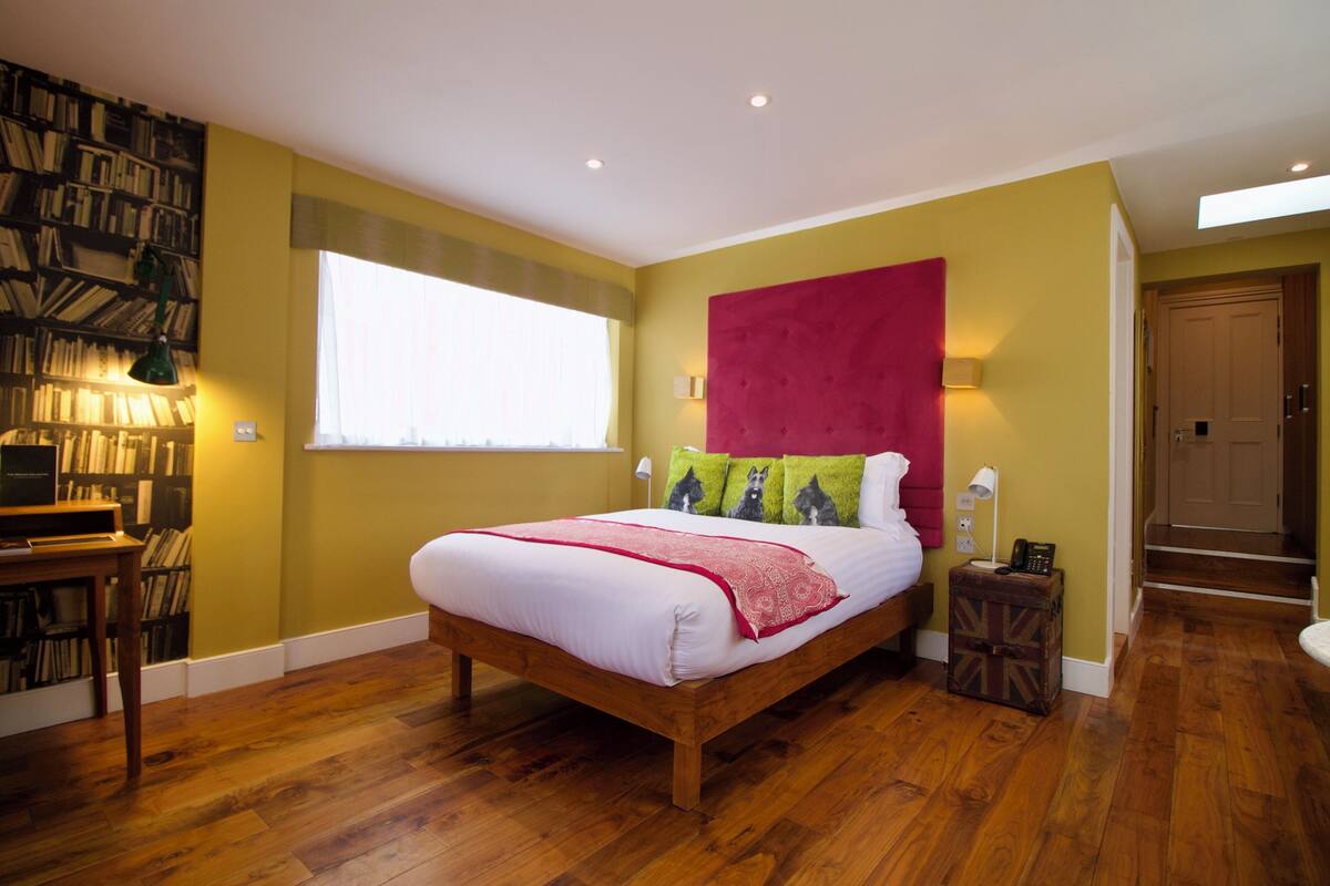 A bedroom with a wooden bed, a bookshelf, and a window with curtains.