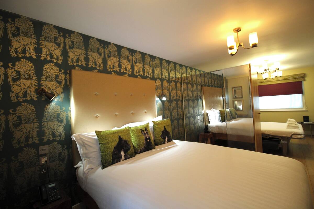 A hotel room with a large bed, a bedside table, a mirror, and a wall with a lion pattern.