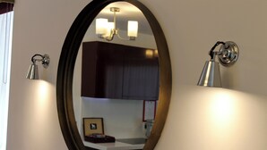 Une salle de bain avec un miroir rond, un luminaire fixé au mur et un plafonnier.