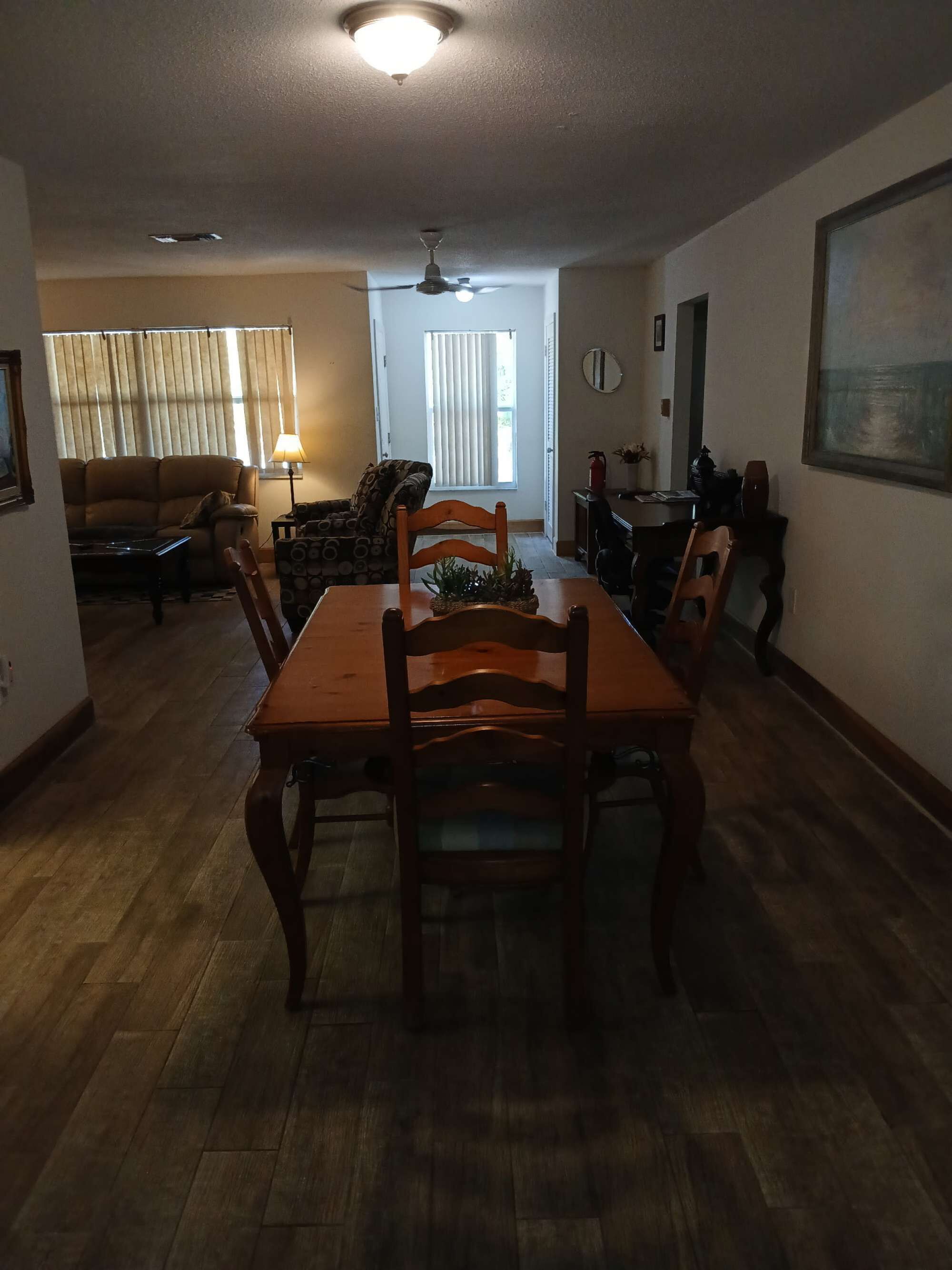 Uma área de refeições com uma mesa e cadeiras de madeira, um ventilador de teto e uma janela com persianas.