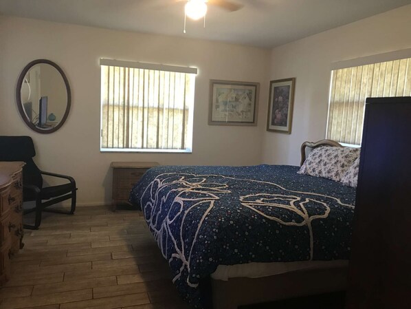 A bedroom with a bed, a dresser, a chair, a window with blinds, and a ceiling fan.