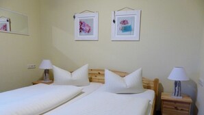 Una habitación con dos camas, cada una con almohada y lámpara de noche. Hay cuadros en la pared.