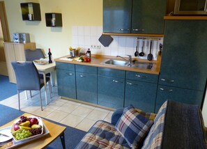A compact kitchen with a sink, stove, and cabinets. There is a dining area with a chair and a table. - 2-room apartment on the upper floor with sunny balcony - Ferienhaus am Schmachter See (Binz)