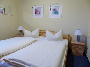 A room with two beds, each with a pillow and a bedside lamp. There are framed pictures on the wall. - 2-room apartment on the upper floor with sunny balcony - Ferienhaus am Schmachter See (Binz)