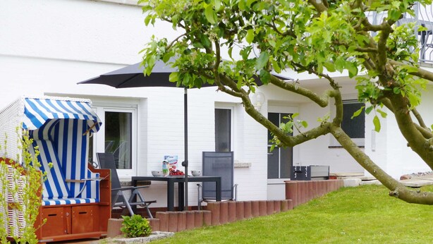 Un patio con un paraguas a rayas, una mesa con cuencos y un edificio blanco al fondo.