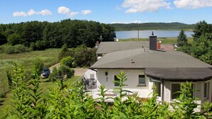 Una casa con un techo grande, una chimenea y vistas a un lago y un bosque.