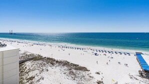 A beach with a sandy shore, a pier in the distance, and a building with a blue roof. - Gulf Shores Beachfront Condo | Sleeps 6 | Gulf-Front Pool & On-Site Dining (Gulf Shores)