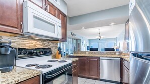 A modern kitchen with a built-in stove, microwave, and stainless steel refrigerator. - Gulf Shores Beachfront Condo | Sleeps 6 | Gulf-Front Pool & On-Site Dining (Gulf Shores)