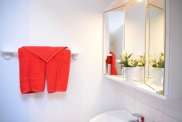 A bathroom with a white sink, a mirror, and a red towel hanging on a towel rack.