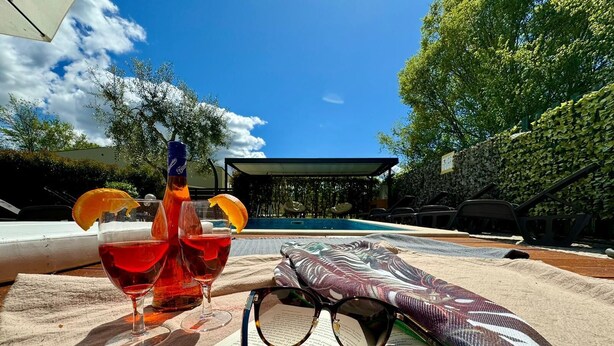 Une scène de bord de piscine avec un livre, des lunettes et des boissons posés sur une serviette.