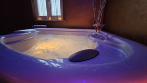 Un bain à remous avec un siège noir et un verre rempli d’un liquide rouge, le tout placé devant un mur avec une fenêtre et une plante.
