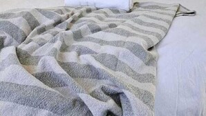 Un lit bien fait, avec une couverture à rayures, une serviette enroulée et un panier tressé suspendu au-dessus.