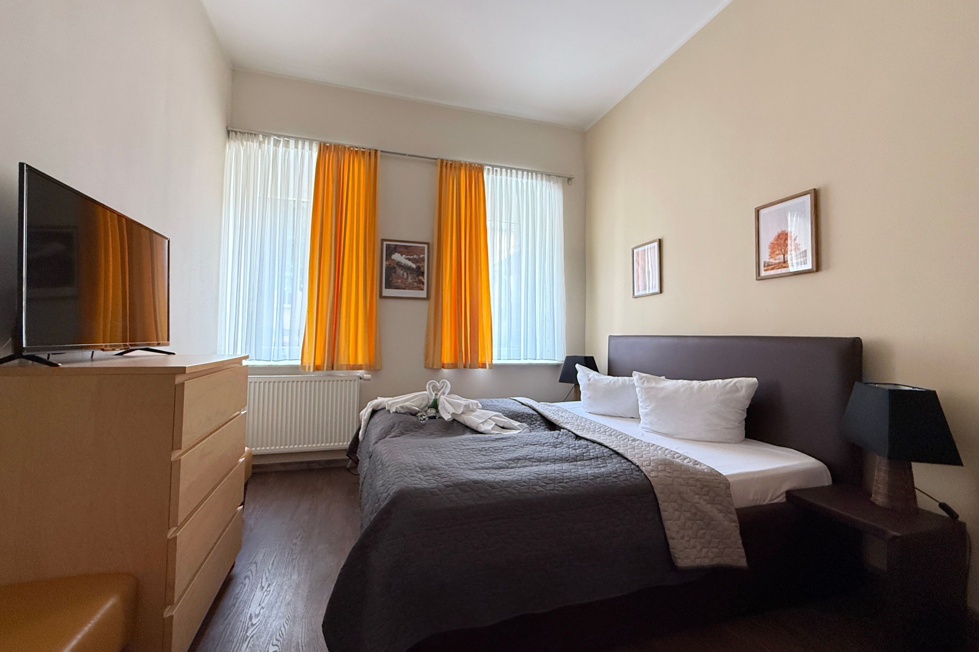 Ein Hotelzimmer mit Bett, Fernseher, Kommode und einem Fenster mit Vorhängen.