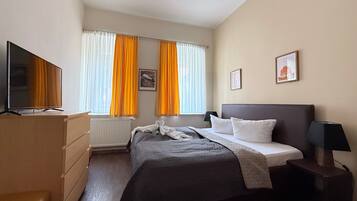 Ein Hotelzimmer mit Bett, Fernseher, Kommode und einem Fenster mit Vorhängen.