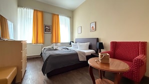 Ein Hotelzimmer mit Bett, Schreibtisch, Stuhl, Nachttisch und einem Fenster mit Vorhängen.