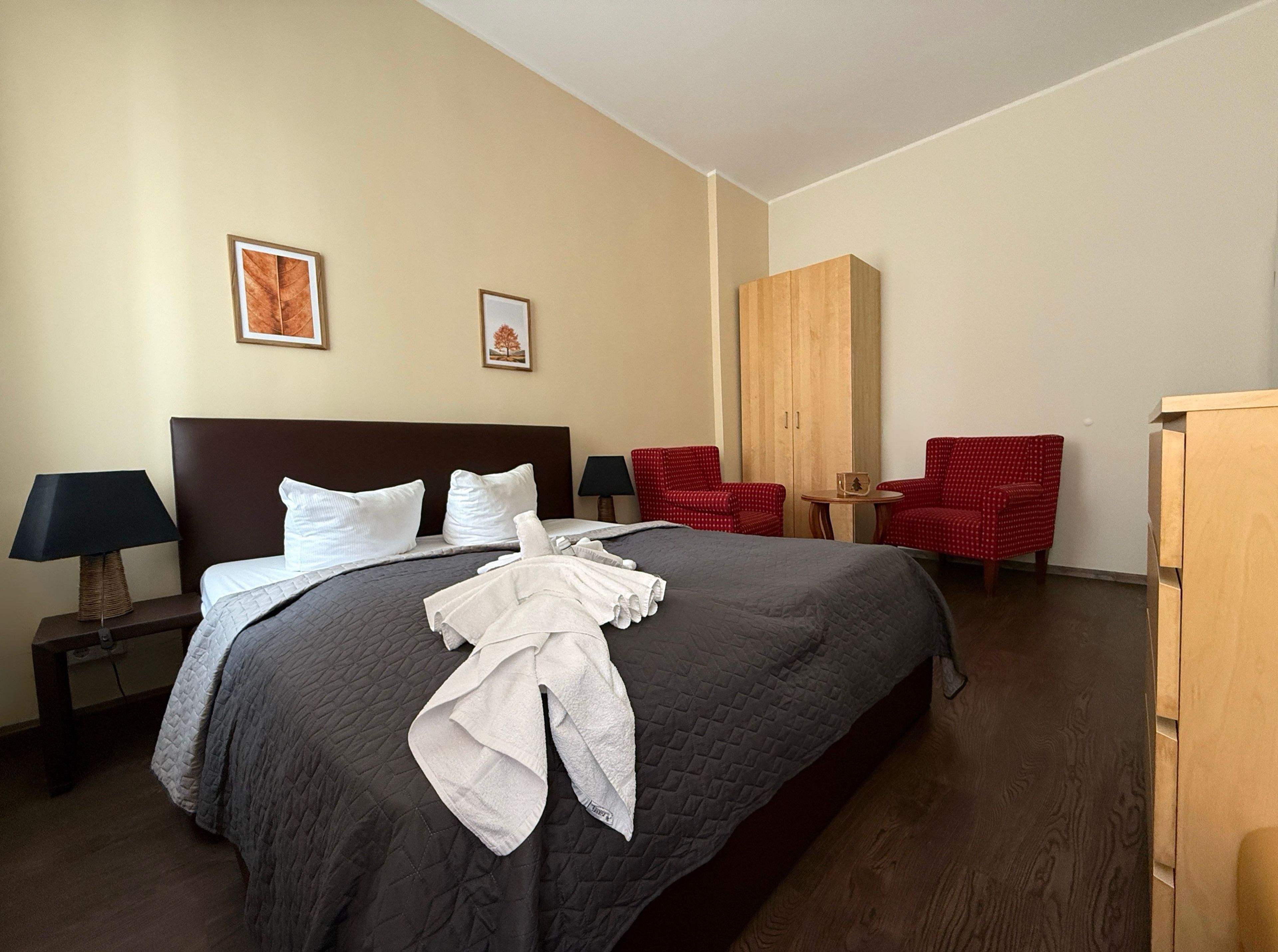 Ein Hotelzimmer mit einem großen Bett, zwei roten Sessel, einem Holzschrank und zwei gerahmten Bildern an der Wand.