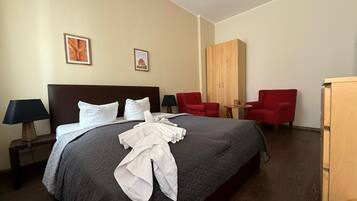 Ein Hotelzimmer mit einem großen Bett, zwei roten Sessel, einem Holzschrank und zwei gerahmten Bildern an der Wand.