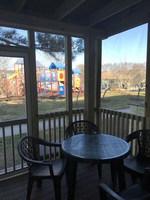 Eine überdachte Terrasse mit Tisch und Stühlen, mit Blick auf einen Spielplatz mit bunten Spielgeräten.