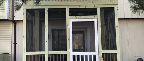 A wooden deck with a white door and windows, surrounded by a fence and a tree.