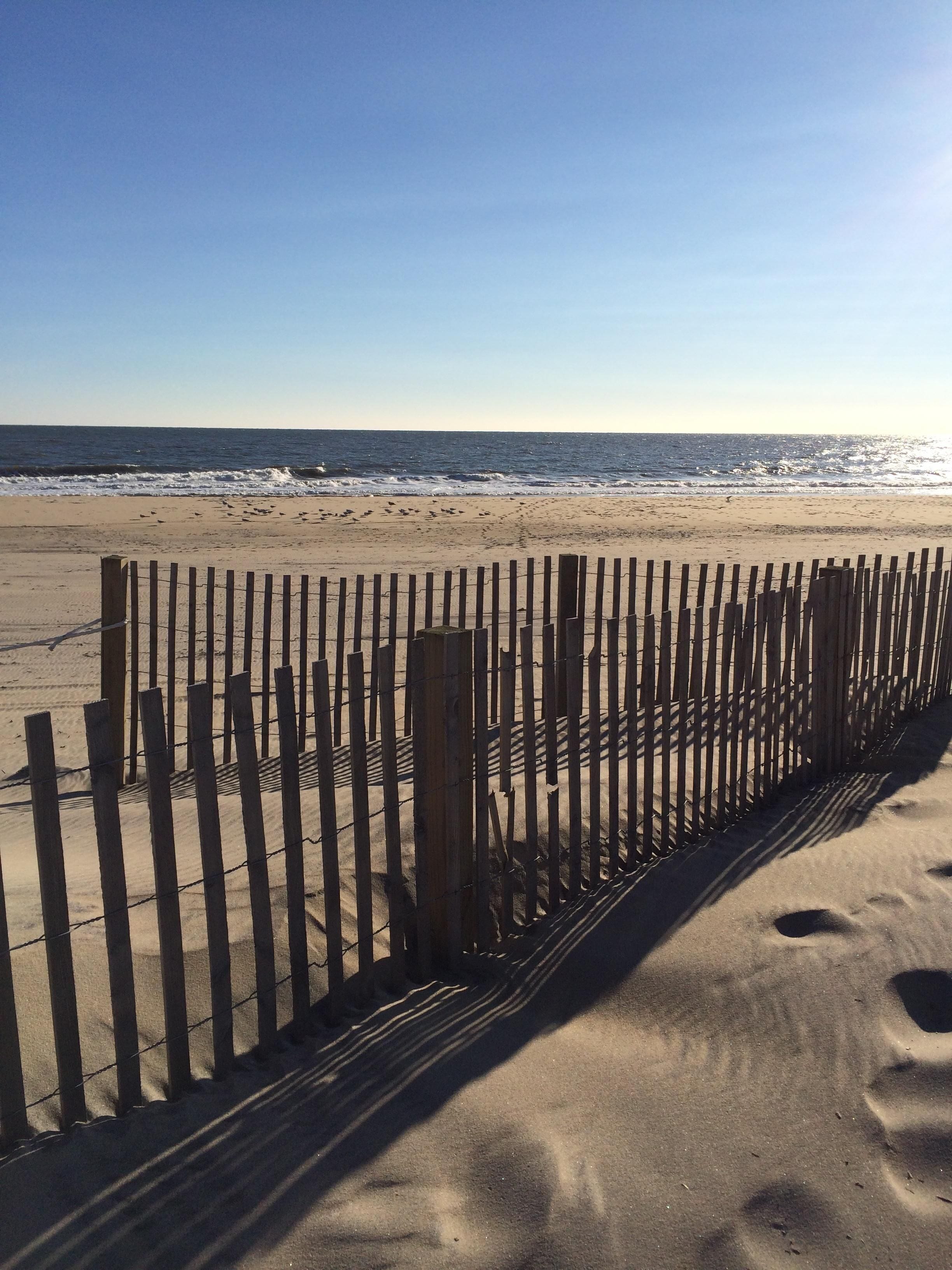A sandy beach with a wooden fence and a clear view of the ocean.