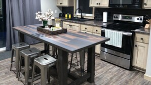 Une cuisine moderne avec des meubles de couleur bois clair, des appareils en acier inoxydable, un îlot central en bois foncé et des tabourets de bar.