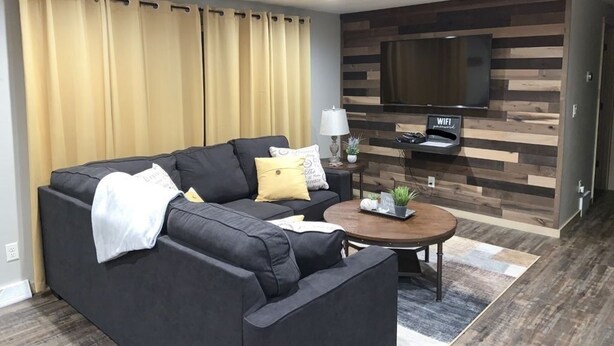 Un salon moderne avec un canapé d’angle, une table basse et un téléviseur à écran plat fixé à un mur en bois.