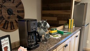 Une cuisine avec des meubles de rangement en bois, une machine à café, des tasses et une horloge au mur.