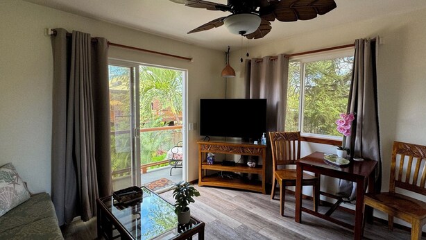A living room with a glass coffee table, wooden chairs, a TV on a wooden stand, and a ceiling fan. - 1 Bdrm Ocean View walk to Turtle Beach, close to Kona Village&Magic Sands Beach (Kailua)