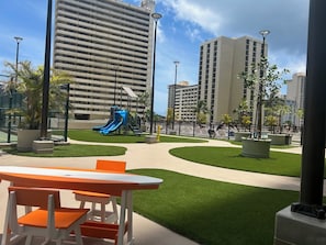 A playground with slides and a fenced area, surrounded by buildings and greenery.