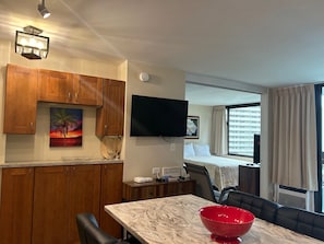 A compact hotel room with a dining area, a TV mounted on the wall, and a large window with curtains.