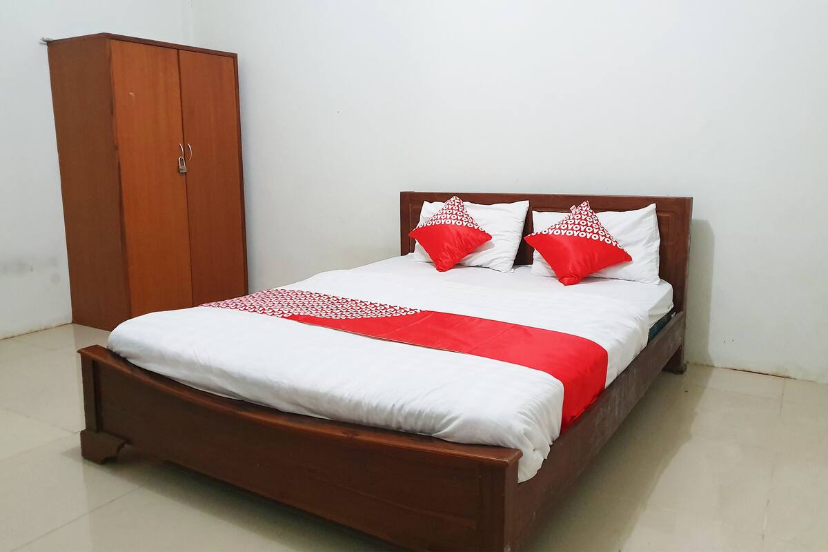 A bed with white and red bedding, a wooden wardrobe, and a plain white wall.