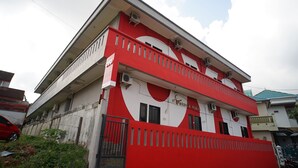 A two-story building with a red and white facade, multiple balconies, and air conditioning units.
