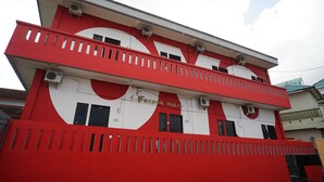 A multi-story building with a red and white facade, featuring a balcony on the upper level and several windows.