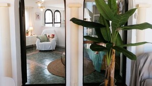 A room with a white chair, a round woven rug, and a large green plant. - A13 CONSULADO A 5º 3 (Calpe)