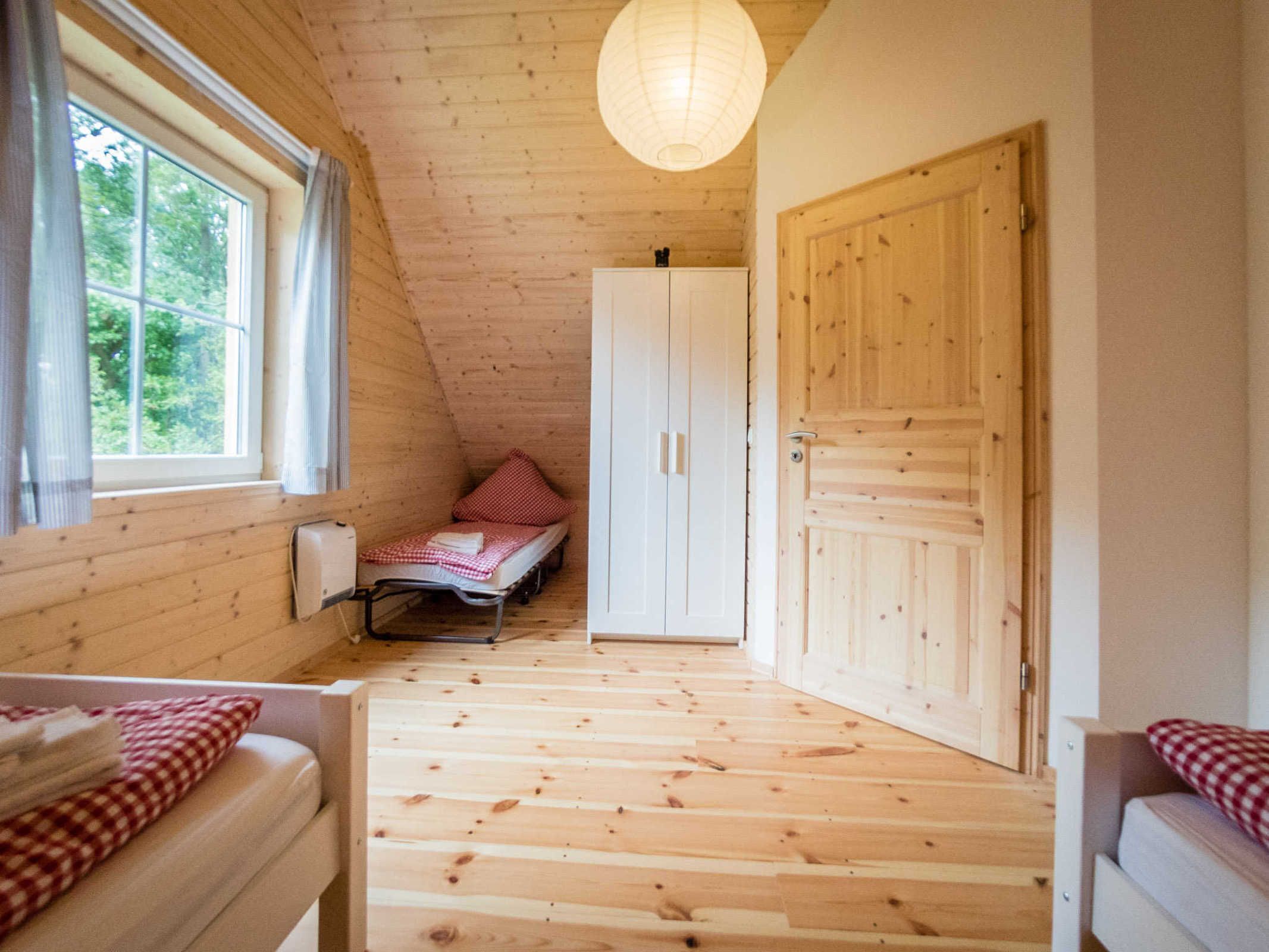 Ein gemütlicher Raum mit Holzwänden und -böden, einem Einzelbett, einem Kleiderschrank und einem Fenster mit Vorhängen.