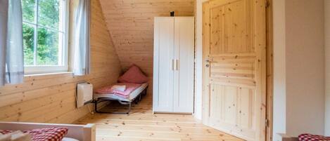Ein gemütlicher Raum mit Holzwänden und -böden, einem Einzelbett, einem Kleiderschrank und einem Fenster mit Vorhängen.