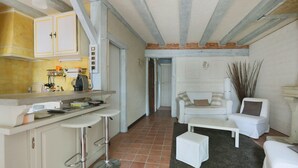 Un espacio habitable compacto con área de cocina que incluye un conjunto de taburetes de bar y una mesa de comedor. Un sofá blanco y una pequeña mesa blanca se encuentran en la sala.