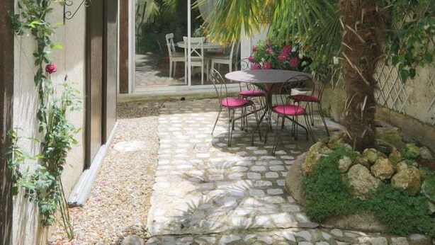Un patio con un sendero de piedra, una mesa de madera con sillas y una zona de patio con cerramiento de vidrio.