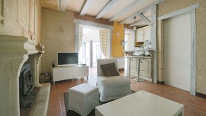 Una sala de estar con chimenea, televisor, sofá y una cocina con armarios y microondas.