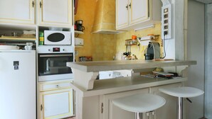 Cocina compacta con armarios blancos, microondas, horno y cafetera.