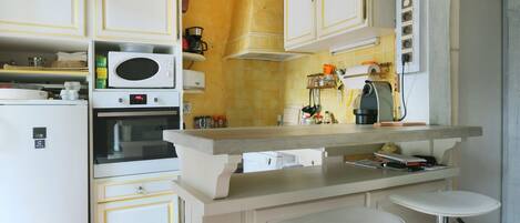 Cocina compacta con armarios blancos, microondas, horno y cafetera.