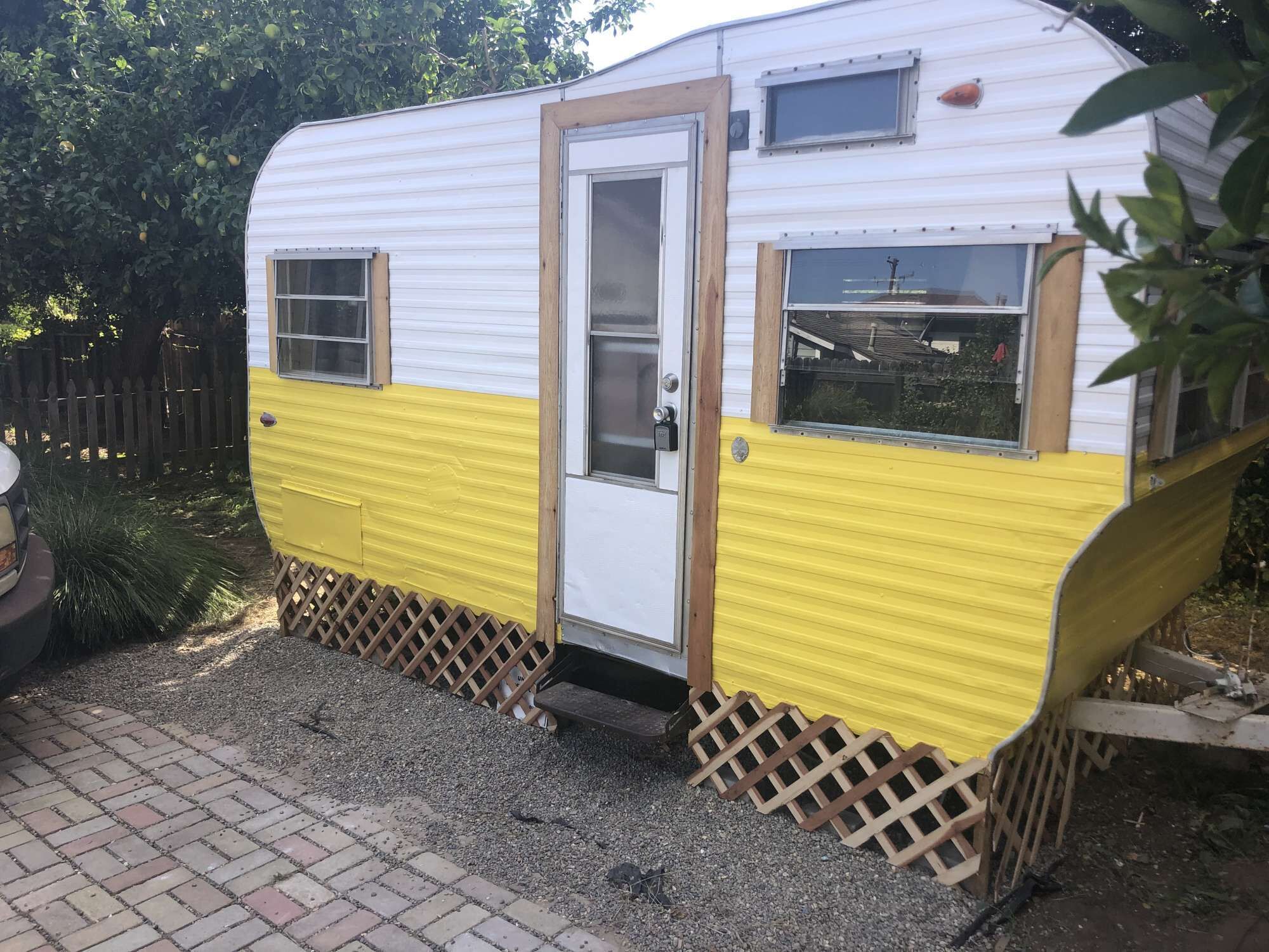 A small, single-story trailer with a white and yellow exterior, a door, and two windows.