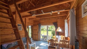 A wooden cabin interior with a dining area, a staircase, and a large sliding glass door leading to an outdoor patio. - House 5 - SCHMIDT'S Cottages in the countryside (Lüdershagen)
