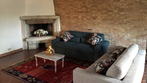 A living room with a brick wall, a fireplace, a sofa, and a coffee table with fruit.