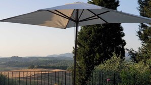 A view from a balcony with a metal railing, overlooking a landscape with hills and trees.