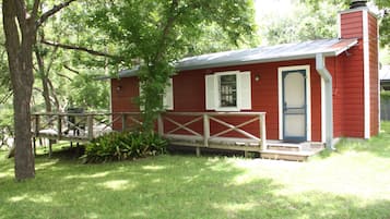 Une cabane rouge avec une terrasse en bois, une porte et une cheminée.